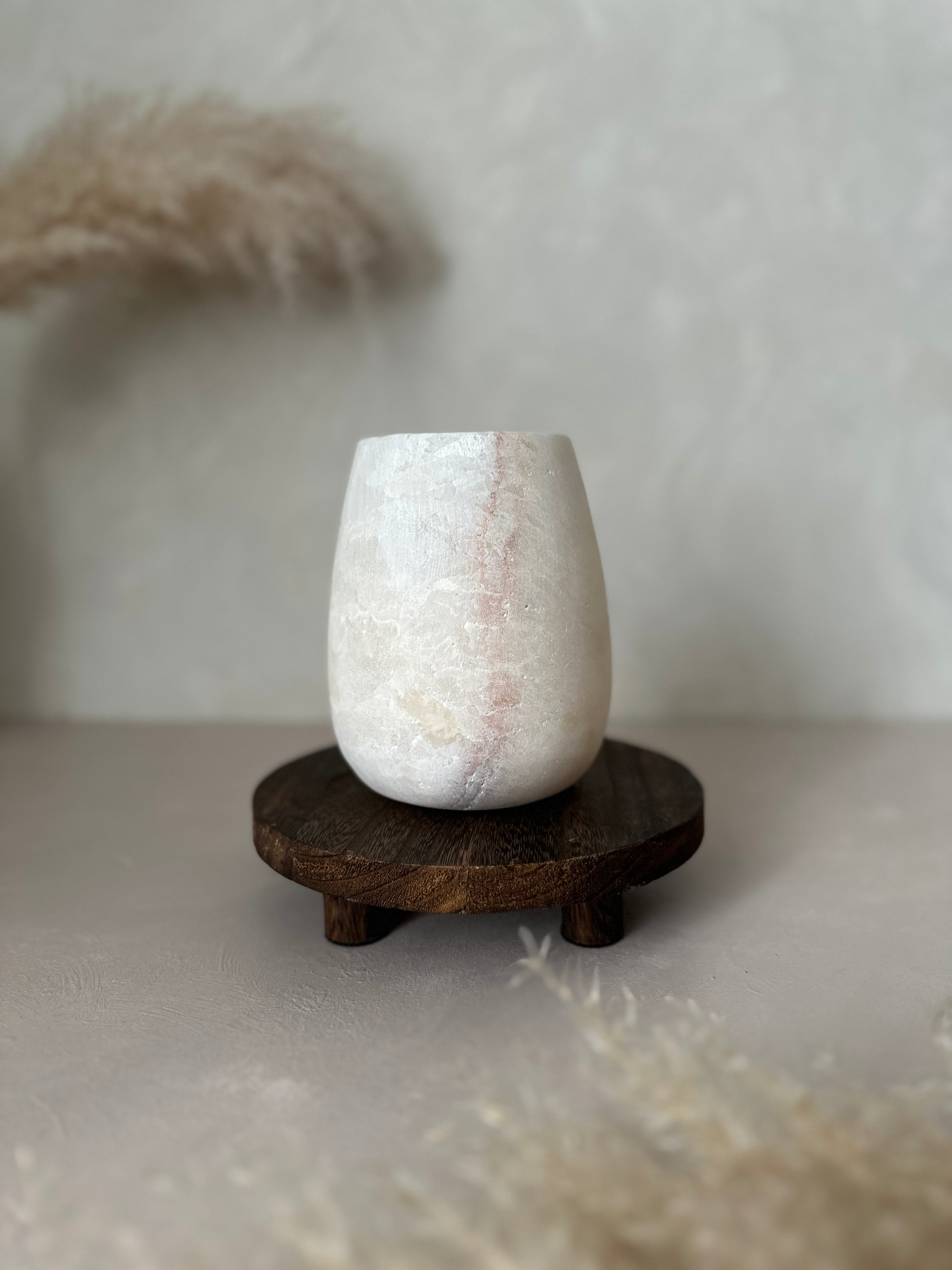 White Alabaster vase on a wooden stand against a neutral background
